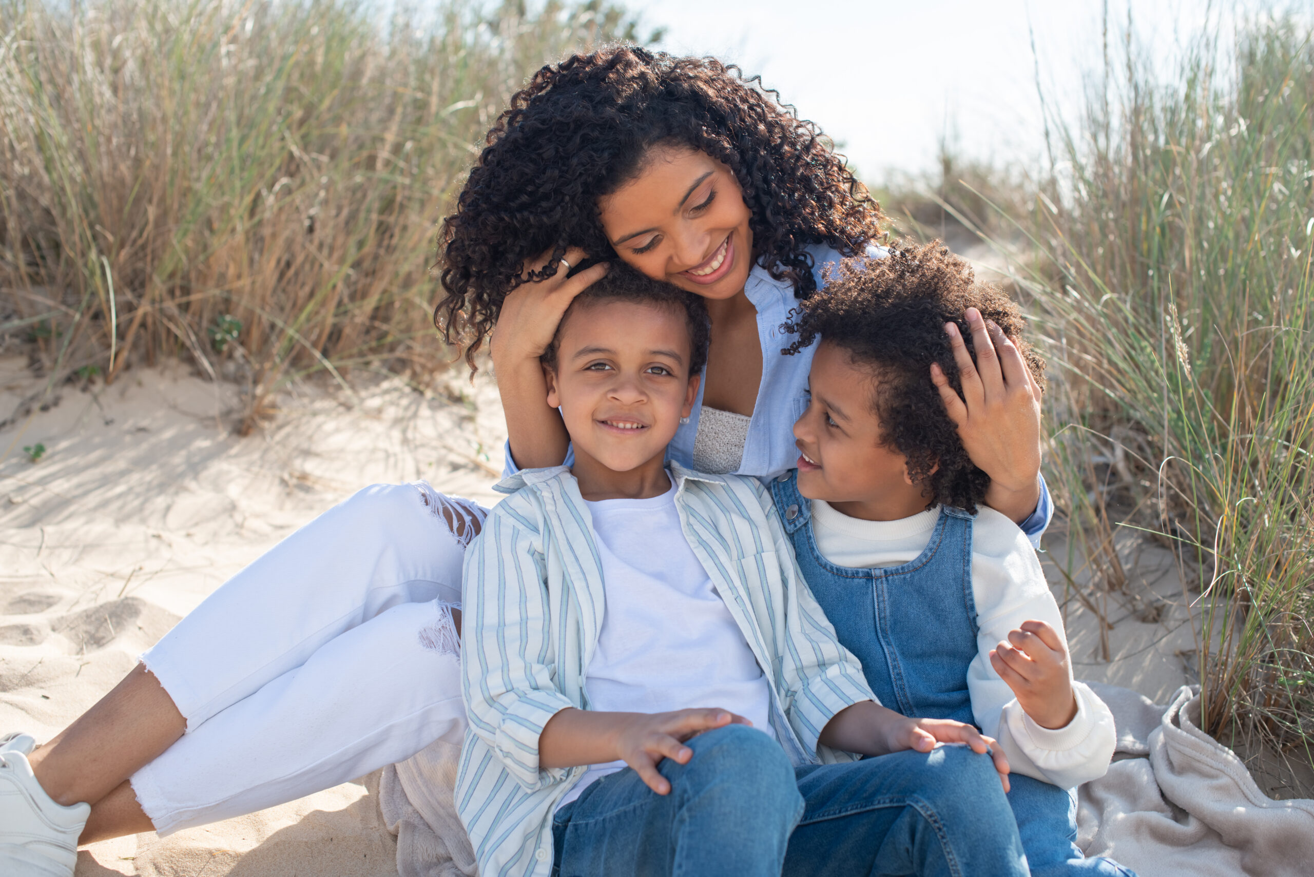 Une jeune maman caresse les cheveux de ses 2 enfants affectueusement sur une plage